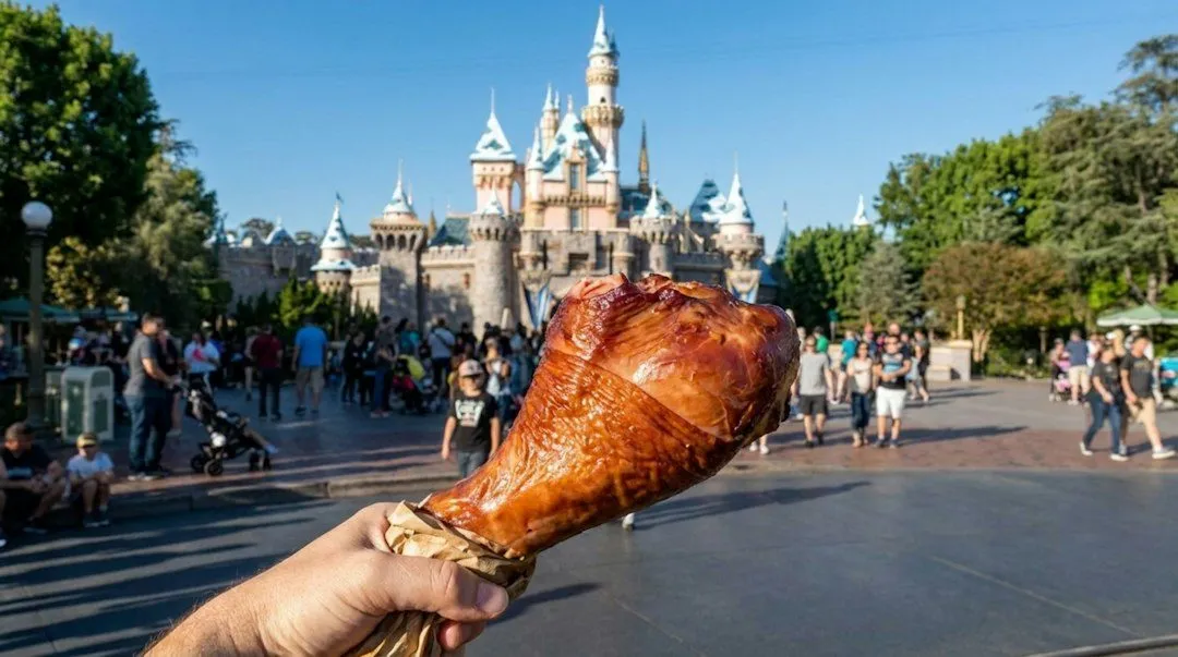 Hand holding turkey leg with castle and crowds in background